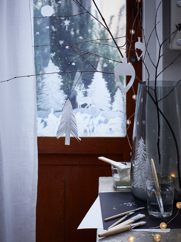 MÅLA set of paint brushes and paint pot are on a table by a door with a painted snow scene; one brush is in a water glass.