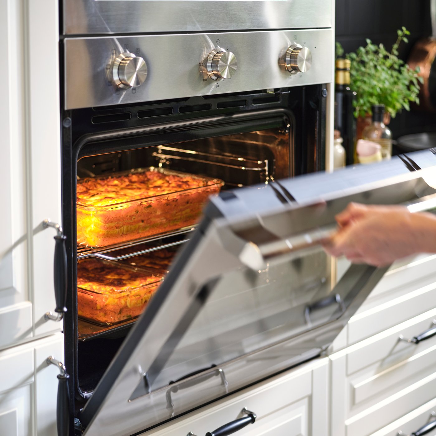 En person åbner ovndøren, så man kan se to fade lasagne, der tilberedes indeni, indrammet af en STENABY varmluftovn i rustfrit stål.