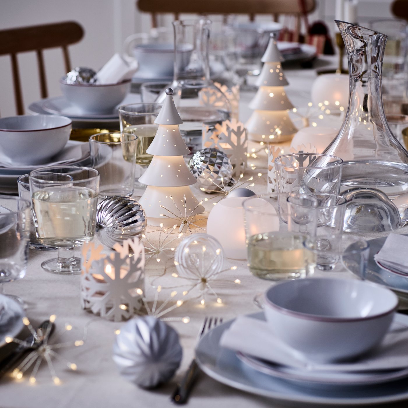 VINTERFINT decorations and STRÅLA lighting are on a festively decorated dinner table in tones of white and silver.