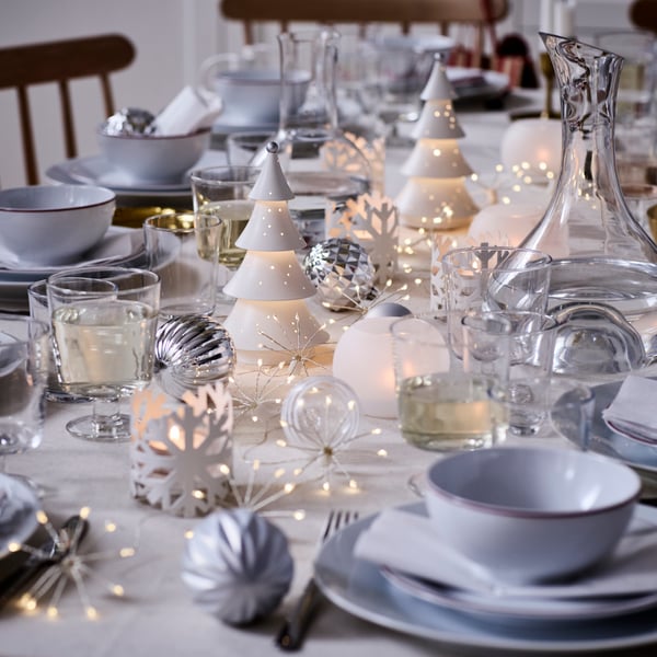 VINTERFINT dekorationer och STRÅLA belysning finns på ett festligt dukat bord i vitt och silver.