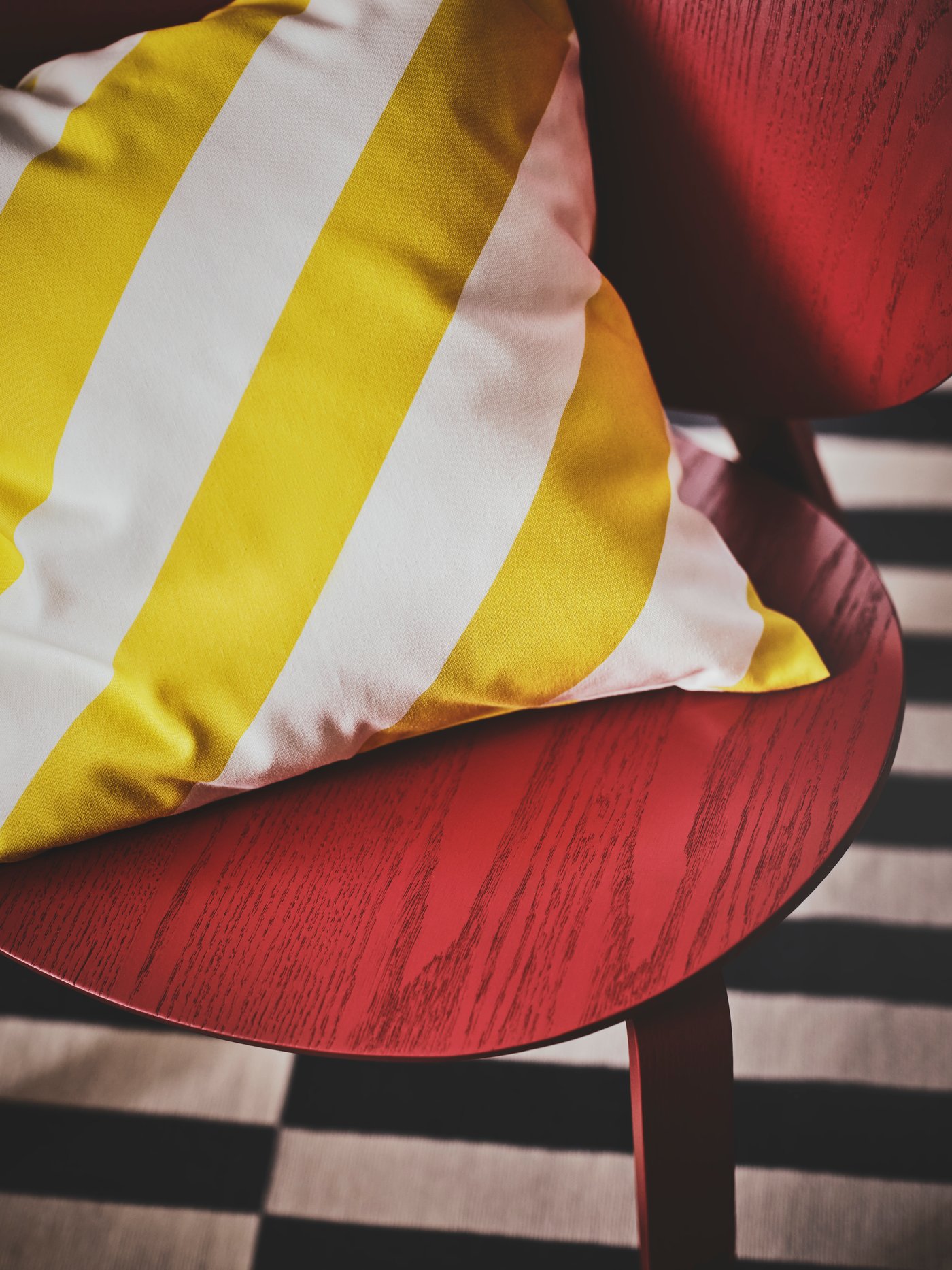 صورة مقرّبة لكرسي أحمر عليه وسادة مخططة باللونين الأصفر والأبيض في الأعلى. تحتها سجادة مخططة بالأبيض والأسود.