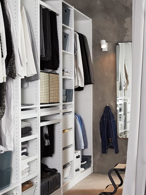 Sypialnia z białą szafą z drewna, stołkiem, prostokątnym lustrem i lampą do czytania.