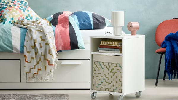 Cama diván BRIMNES con funda de duvet SVALSTJÄRTAR y manta OLIVSPINNMAL con buró VIHALS blanco a un lado.