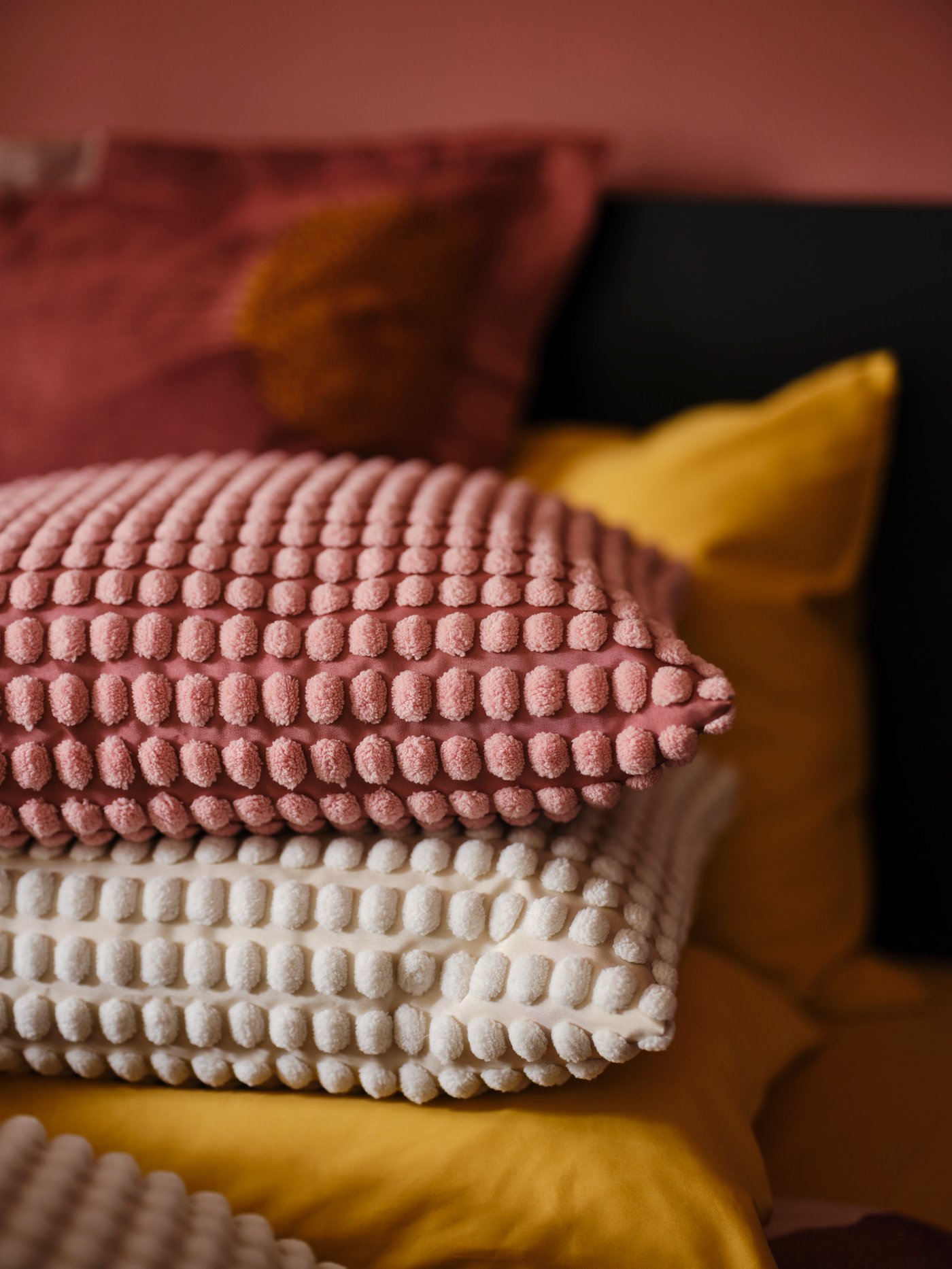 Kaksi koristetyynyä päällekkäin. Toisessa on vaaleanpunainen ja toisessa valkoinen SVARTPOPPEL-koristetyynynpäällinen. 