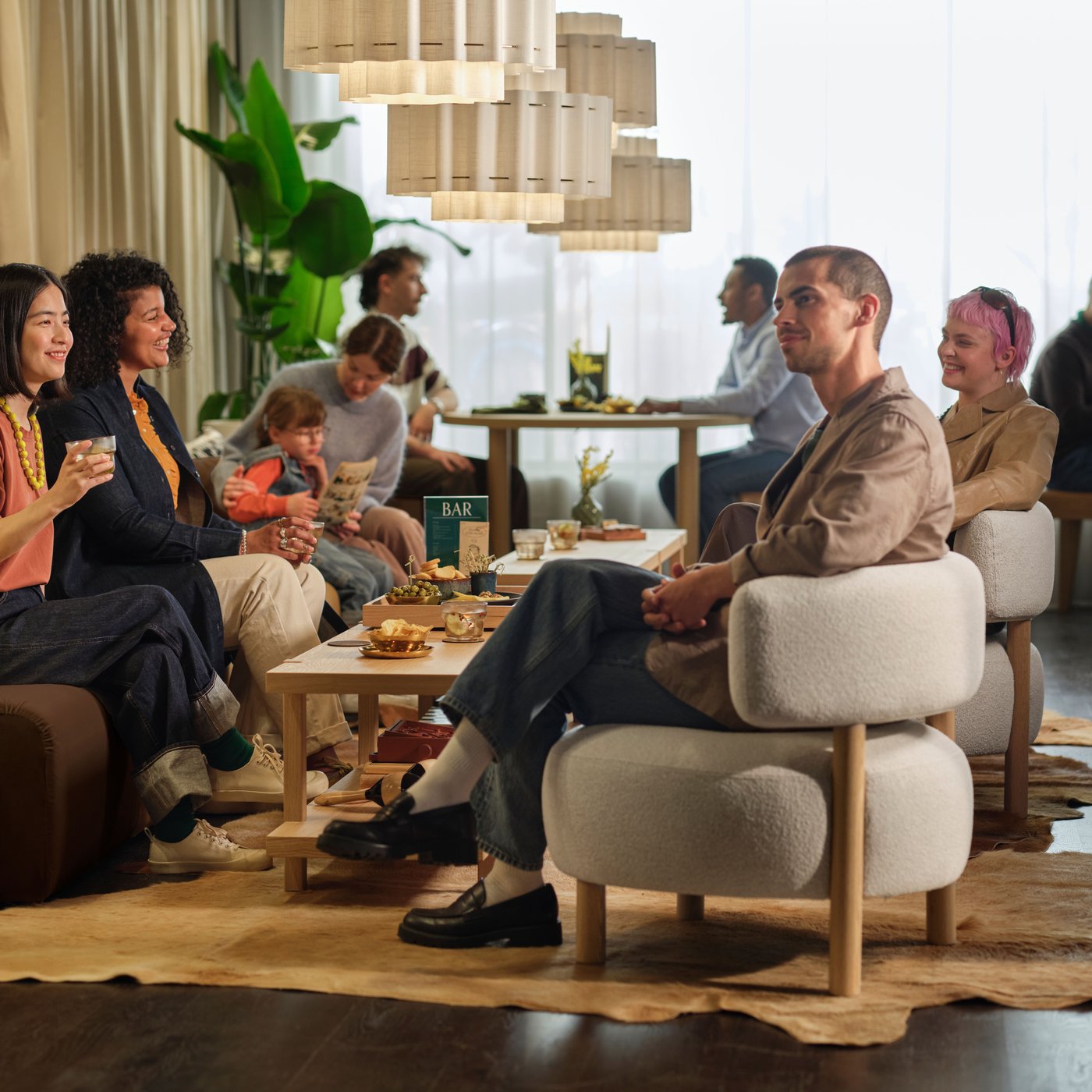 A group of people sit talking in a hotel lobby while sitting on couches and chairs.