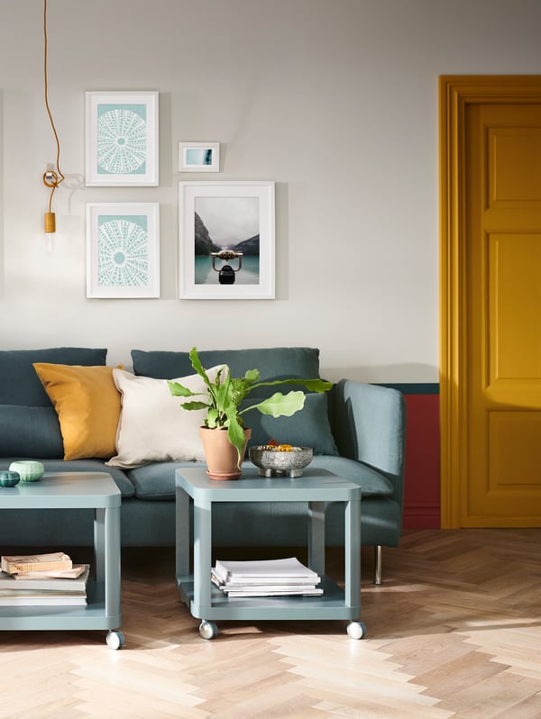 A living room with a teal sofa and two rolling teal carts in front of it.