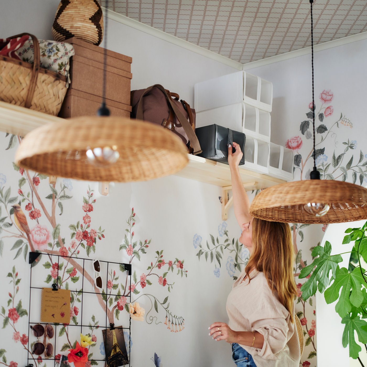 En person sträcker sig upp för att ta ner en mörkgrå SKUBB skokartong från en hylla som också rymmer vita SKUBB skokartonger, korgar och väskor.