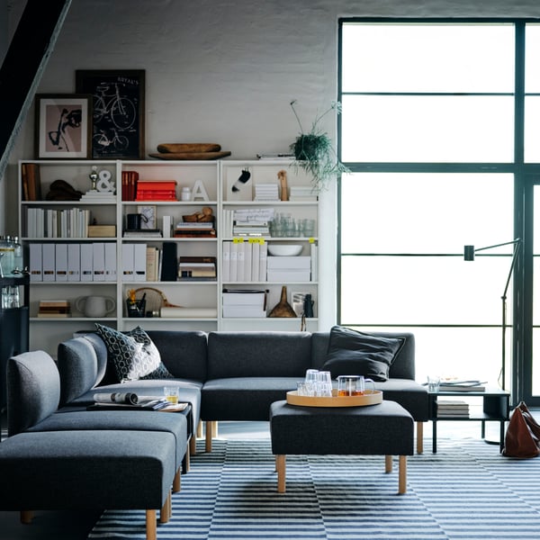 Jasny pokój dzienny z dużym oknem, na środku którego stoi szara sofa modułowa LILLEHEM.