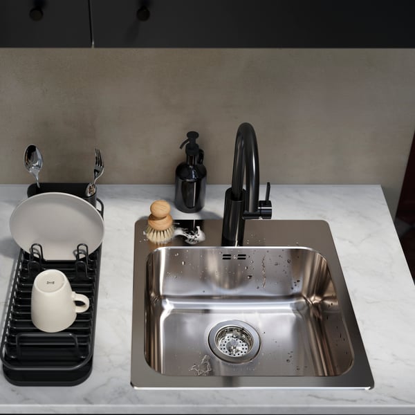 A stainless steel sink with a sleek black tap, a dish rack holding plates and cups, and a stylish soap dispenser.