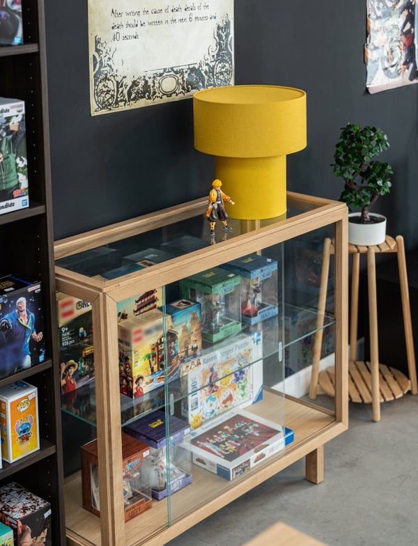 Un vetrina con sopra una lampada da tavolo STOCKHOLM 2025. All'interno della vetrina ci sono delle scatole di LEGO e giochi da tavolo.