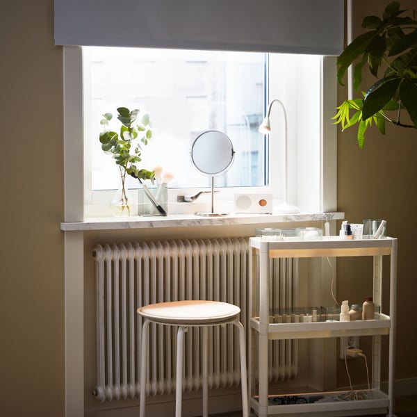 A white VESKEN trolley and a white MARIUS stool stand in front of a window with a TRENSUM mirror on the windowsill.