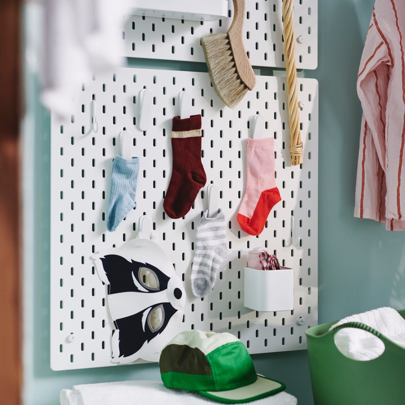 Two square, white SKÅDIS pegboards are on a light green wall, holding single socks in clips and thread spools in a container.