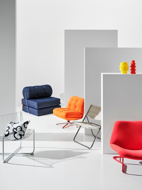 Five different chairs from the Nytillverkad collection are placed in a white room. Among them a blue VÅRKUMLA chair bed.