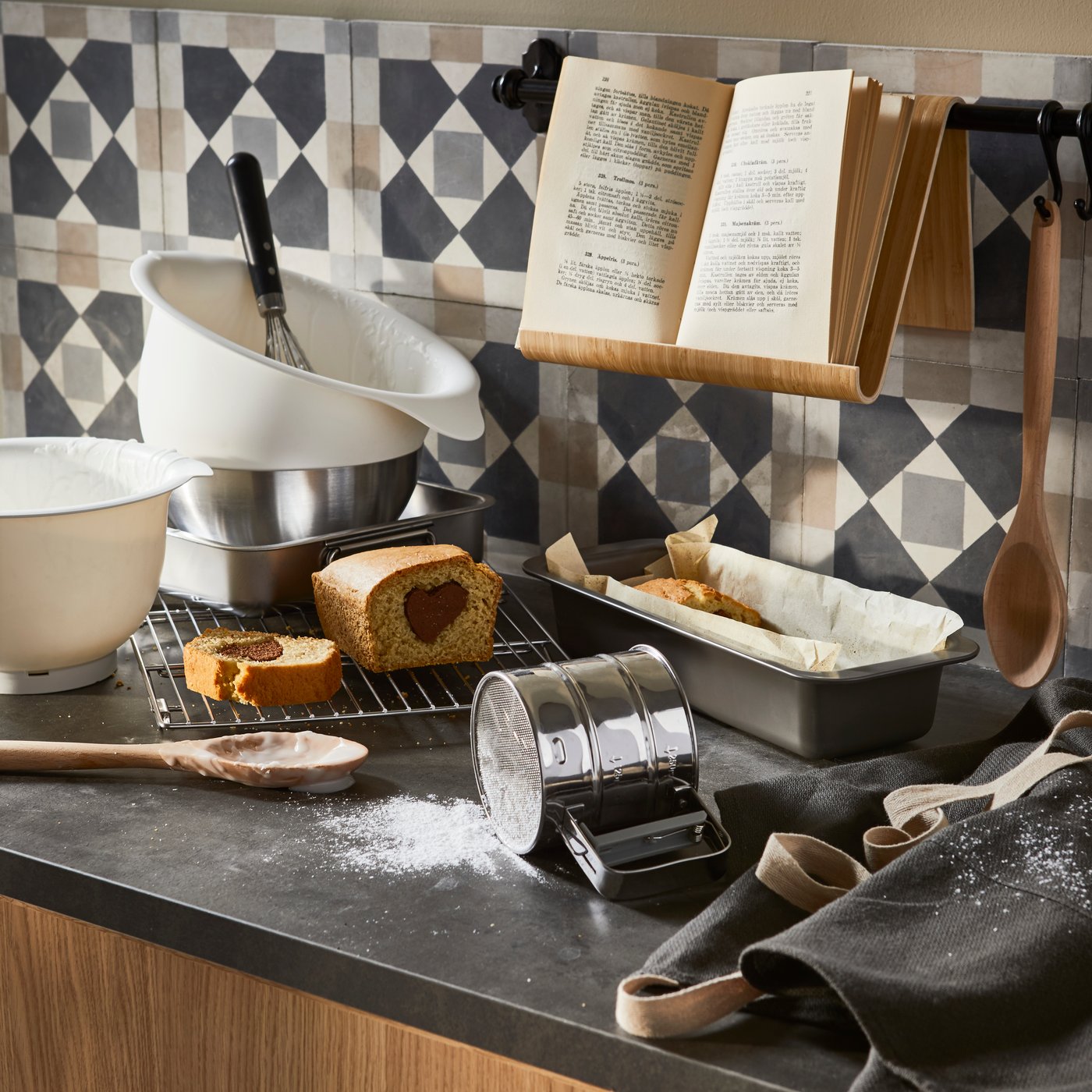 Przesiewaczka do mąki, miski i inne akcesoria do pieczenia na blacie kuchennym.