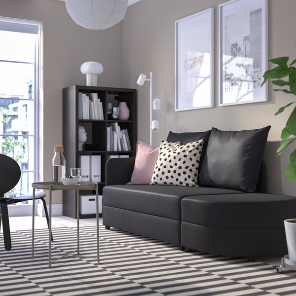 A bright living room with a black-and-white colour scheme, matching the dark-grey LINDÅKRA two-seat sofa-bed at its centre.