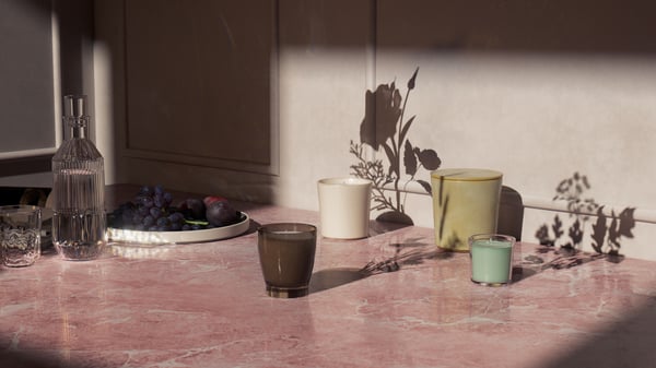A Scandinavian-style dining area with lit ADLAD scented candles and tealights on top of a dining table, by a large window.