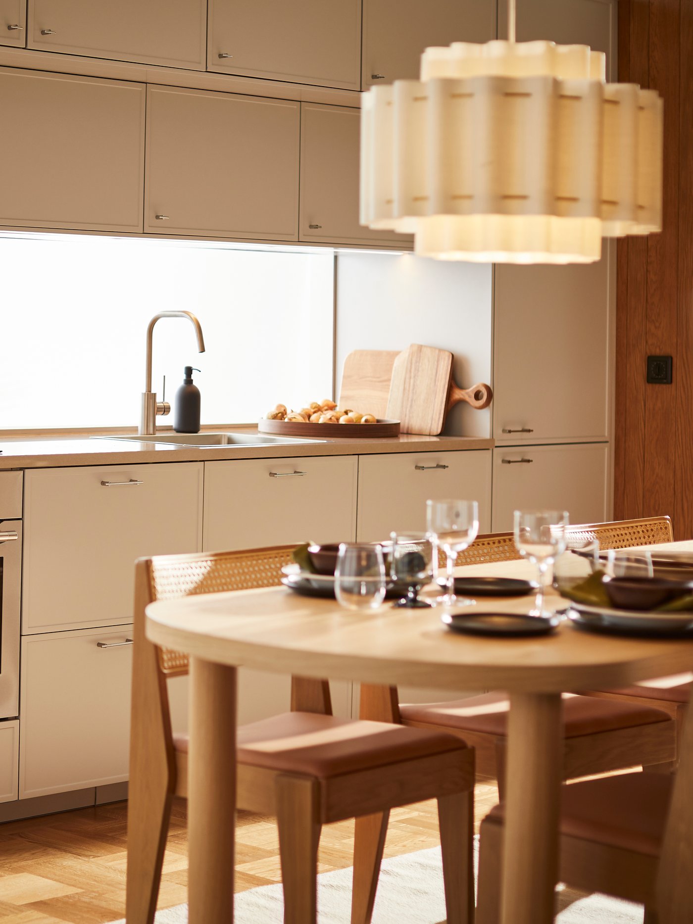 A well-lit, modern Scandinavian kitchen with sleek, light-colored cabinets and a set wooden dining table in the foreground.