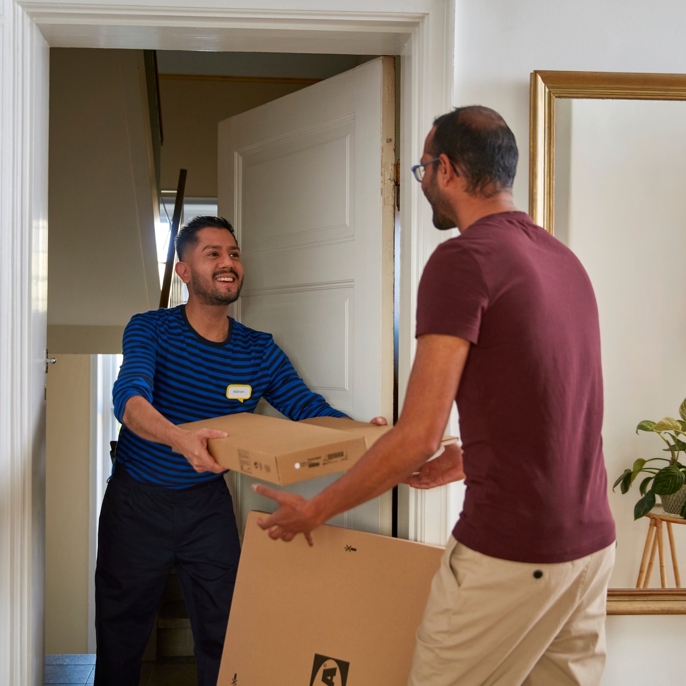 En IKEA medarbejder leverer smilende en pakke til en kunde igennem en åben dør i en lejlighed.