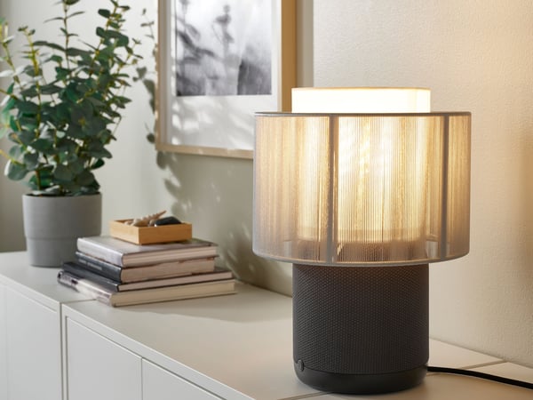 A SYMFONISK table lamp speaker on top of white cabinets, together with some books.