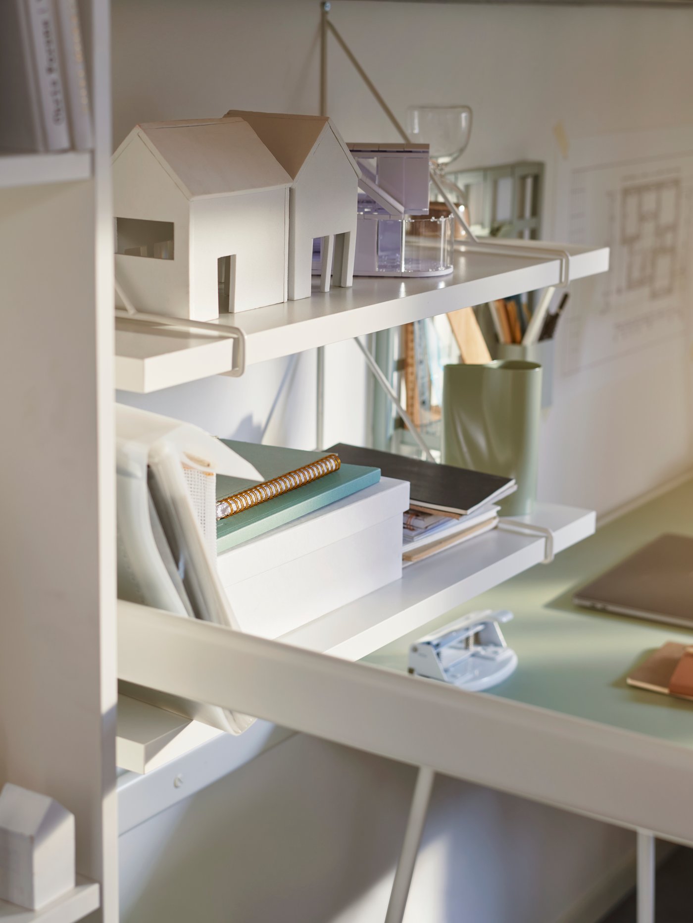 Weiße Hängeregale neben einem Schreibtisch. Darauf sind Blöcke, Schreibutensilien und Deko verteilt.