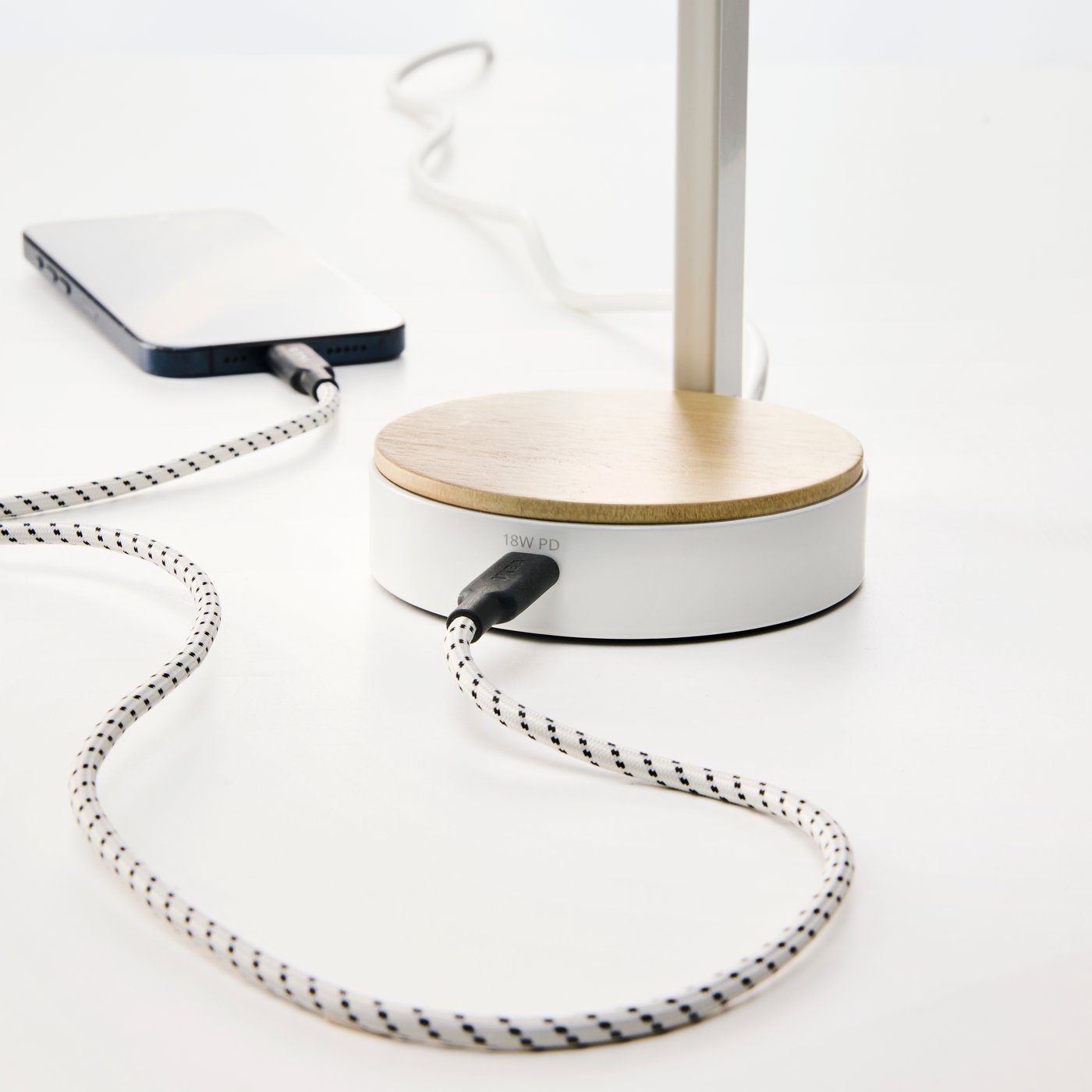 밝은 책상에서 장식 무늬가 있는 USB-C 케이블을 화이트 ENSMÄRKE 엔스메르케 책상등에 연결해 모바일 기기를 충전하는 모습.