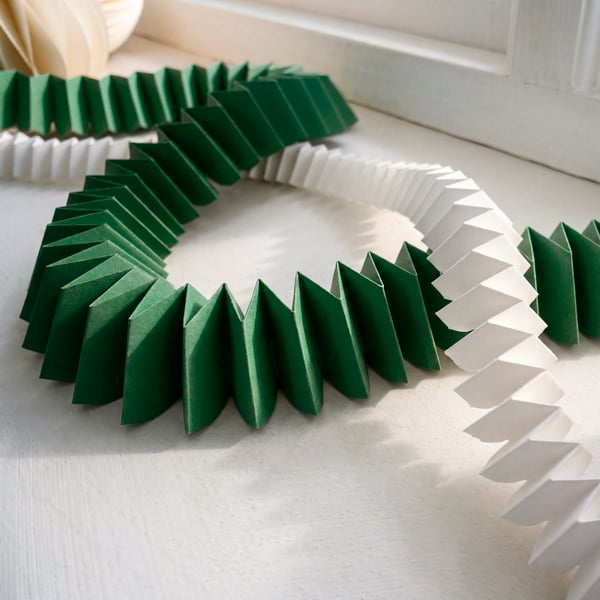 Two VINTERFINT paper garlands in white and green, cross over each other on a windowsill.
