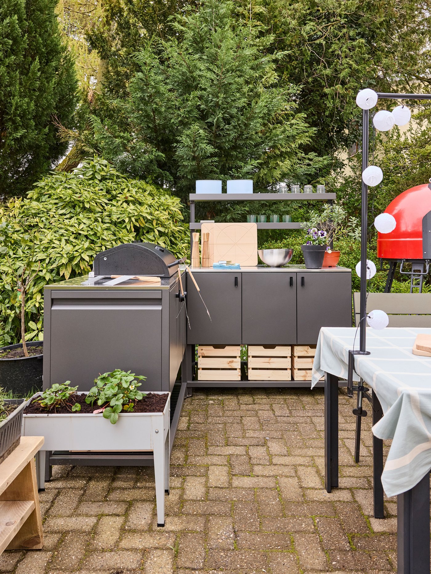 Buitenkeuken met barbecue en opbergkast op terras, omringd door planten en tuinmeubilair voor koken en eten in openlucht.