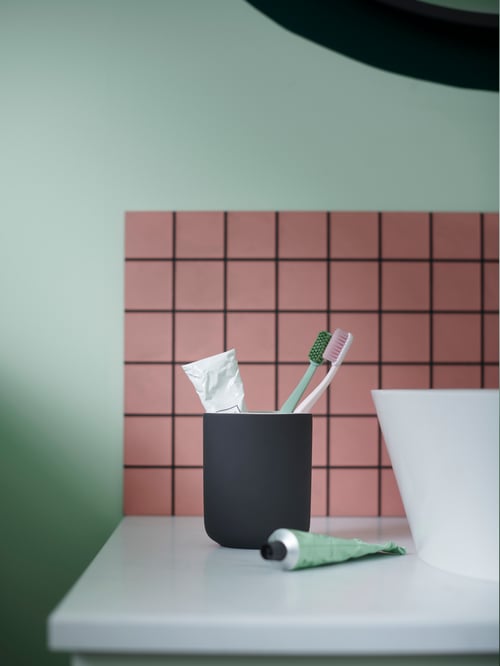 Red tiled bathroom with white table, green wall, toothbrush holder, two toothbrushes, two toothpastes, and one white faucet.