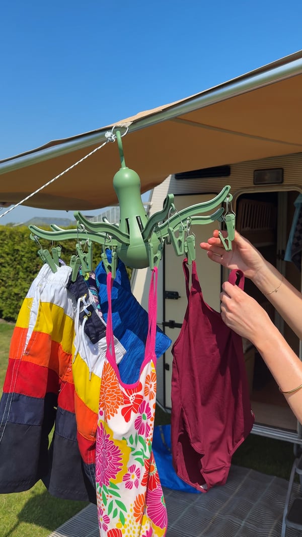A green PRESSA hanging dryer is attached to the side of a tent, while someone hangs swimwear on it.