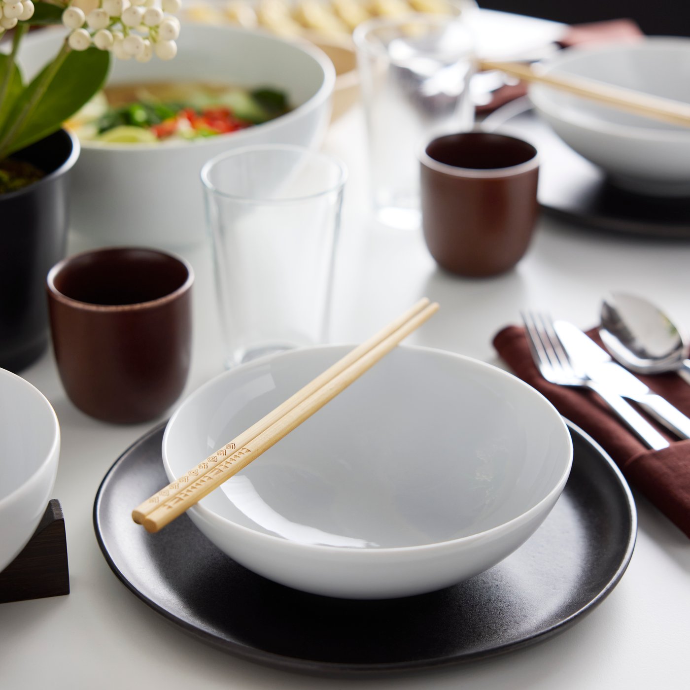 Deux baguettes posées sur un bol IKEA 365+, lui-même posé sur une assiette STOCKHOLM 2025 noire à côté d’un verre IKEA 365+.