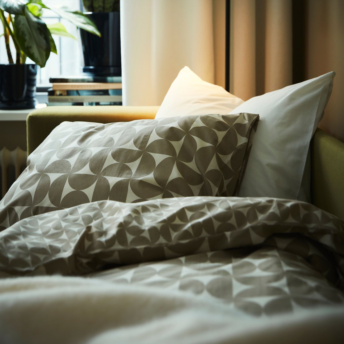 Part of a yellow-green SKÖNABÄCK 2-seat sofa-bed, used as a bed, with grey-beige/off-white ÄNGSNEJLIKA bed linen.