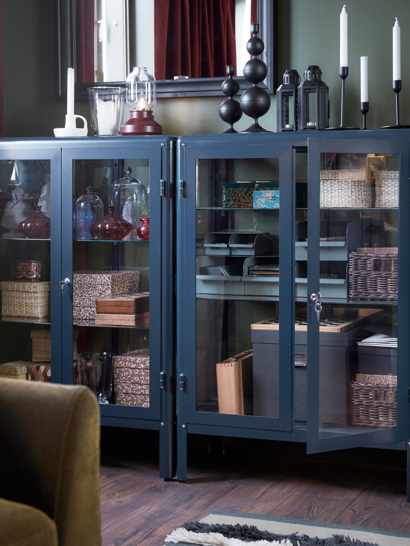 Salón con vitrinas azules en las que hay cajas de almacenaje. Sobre ellas hay candelabros, un farolillo para vela pequeña y una lámpara de mesa.