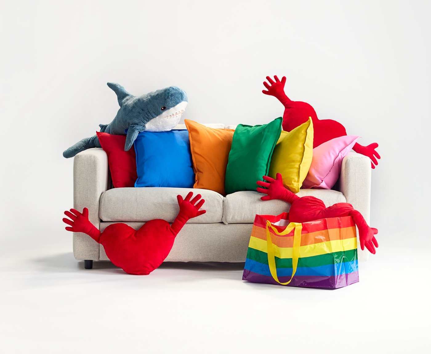 A couch with a BLÅHAJ soft toy, three AMNIG HJÄRTA's and a STORSTOMMA  rainbowbag