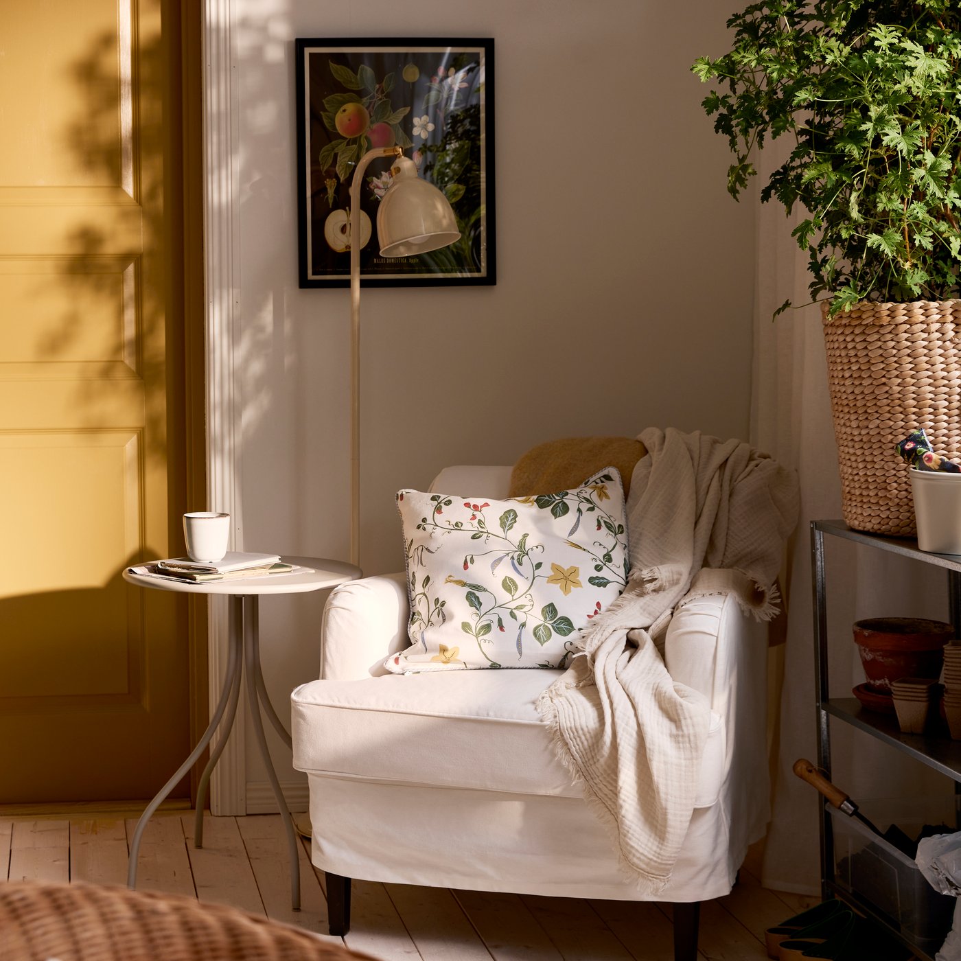 Corner of a room with a white ROCKSJÖN armchair with a side table and reading lamp, and green plant on the other side.