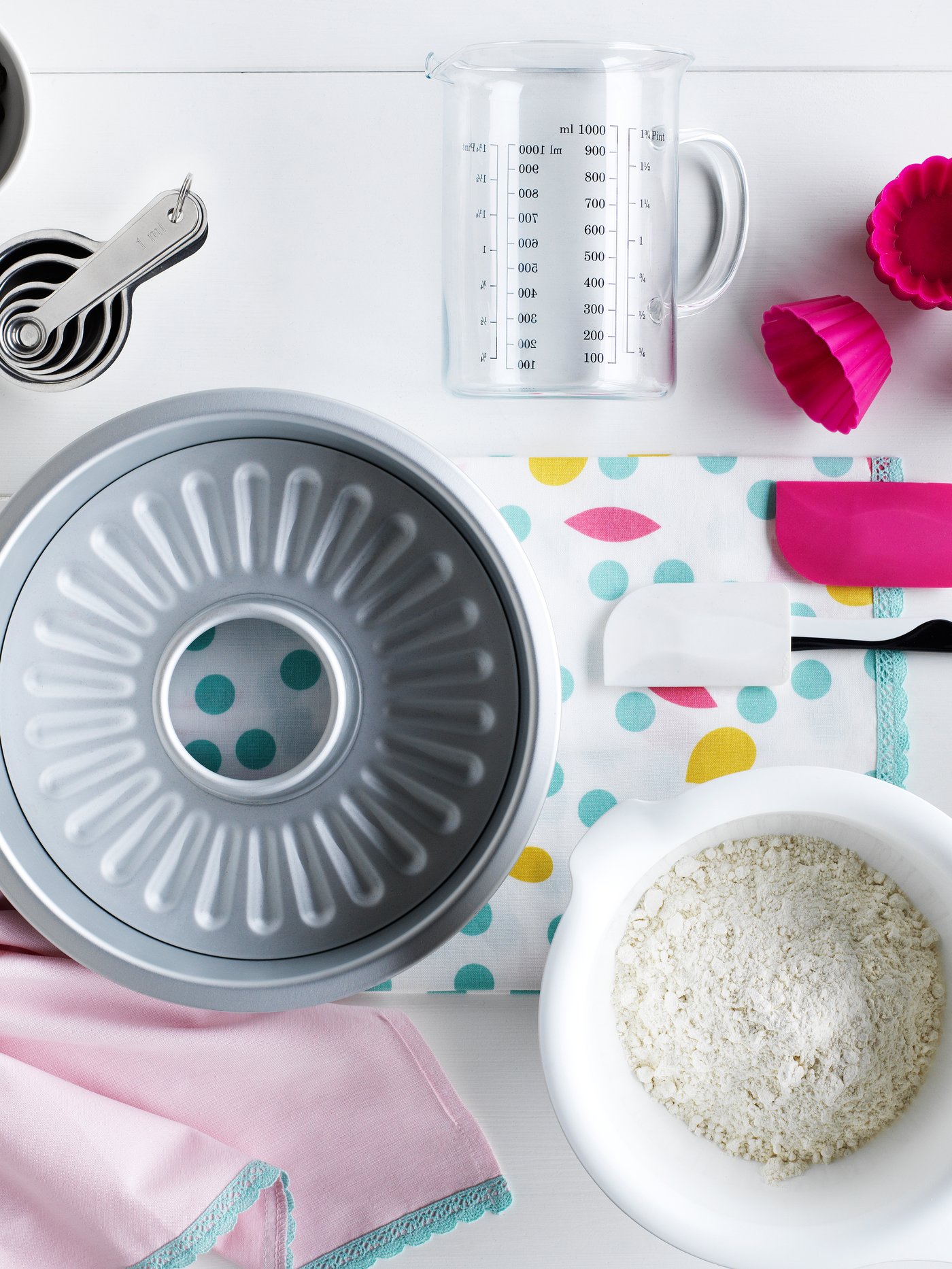 Utensilios de repostería, como molde para queque, medidor y recipiente blanco con mezcla.