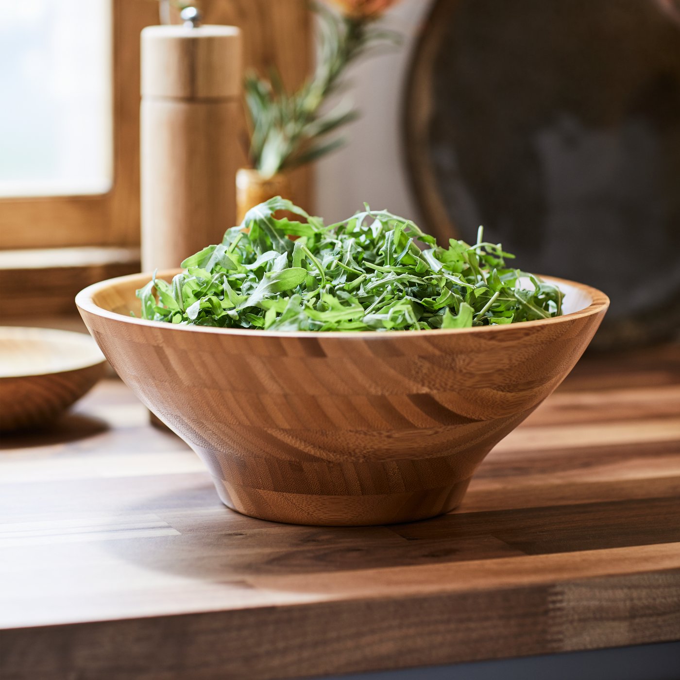 Wooden bowl filled with fresh leafy greens on a kitchen countertop.