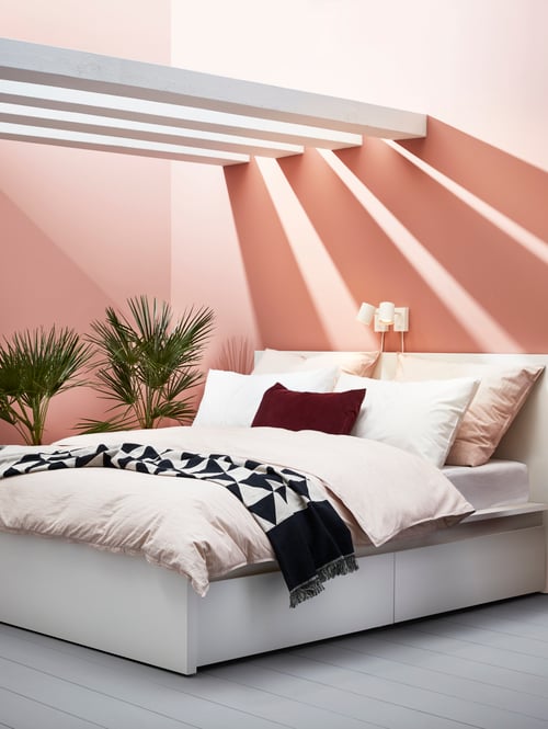 Bedroom with four beams set above a bed frame with storage boxes below, multiple cushions and a throw on the bed.