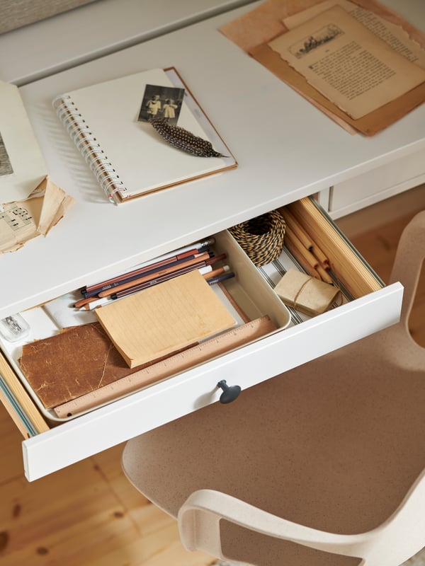 White stain HEMNES desk with two drawers holding plastic/beige NOJIG organiser keeping different stationery in place.