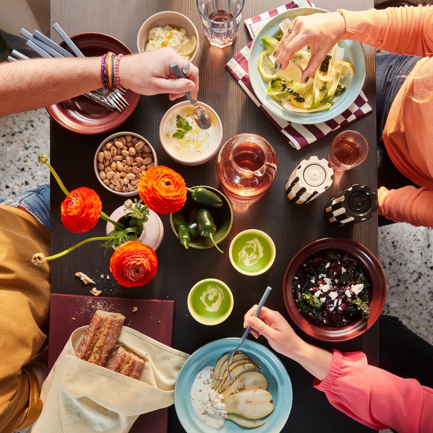 A top shot of a dining table with people eating from the SPJUTLILJA bowls and plates and drinking from the yellow cups.