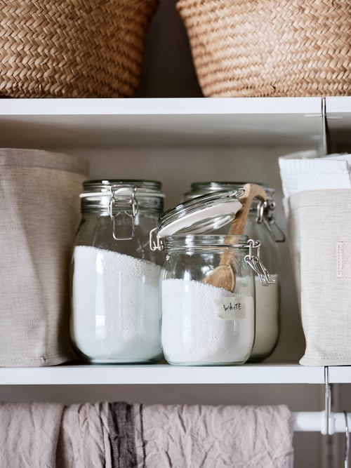 A modern laundry room that features three glass jars with lids and two baskets on the shelves of a wardrobe combination.
