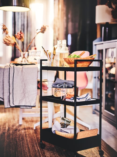 Modern living room with versatile black steel trolley on castors used as a food cart, with cookware and utensils.