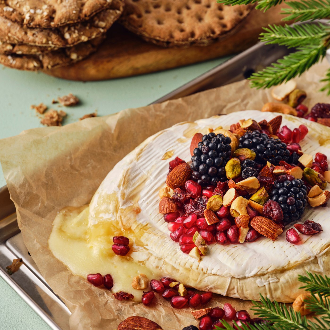 Baked brie garnished with nuts, berries and pomegranate seeds on a baking tray.