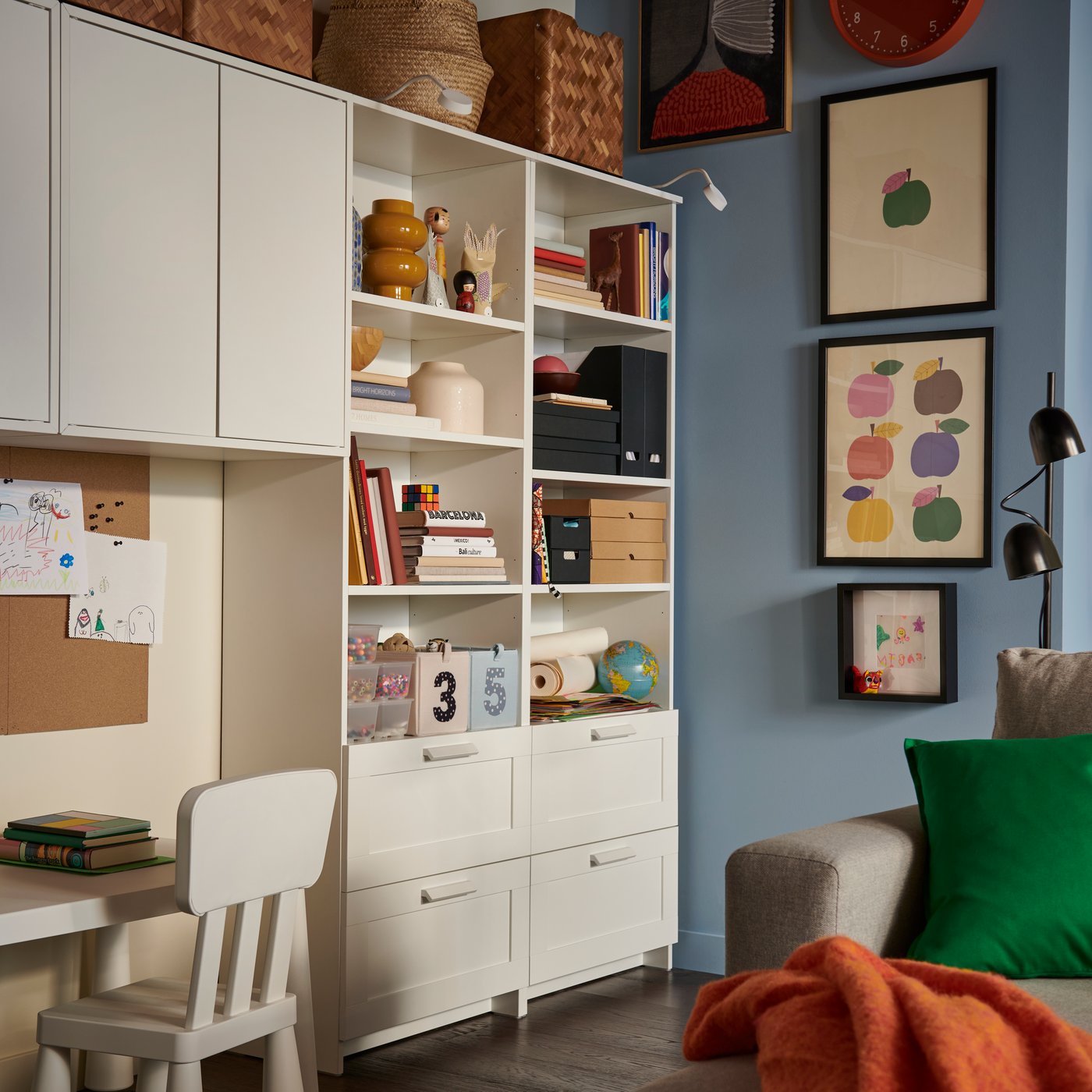 A white BRIMNES bookcase filled with books and decorative boxes, flanked by a children’s deskspace with a matching chair.