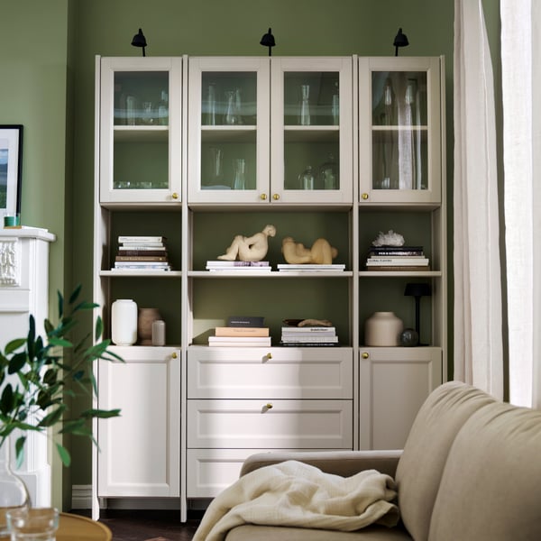 Soggiorno verde con composizione contenitore GULDDRAGARE, con scaffali e mobili chiusi riempiti di libri e oggetti decorativi.