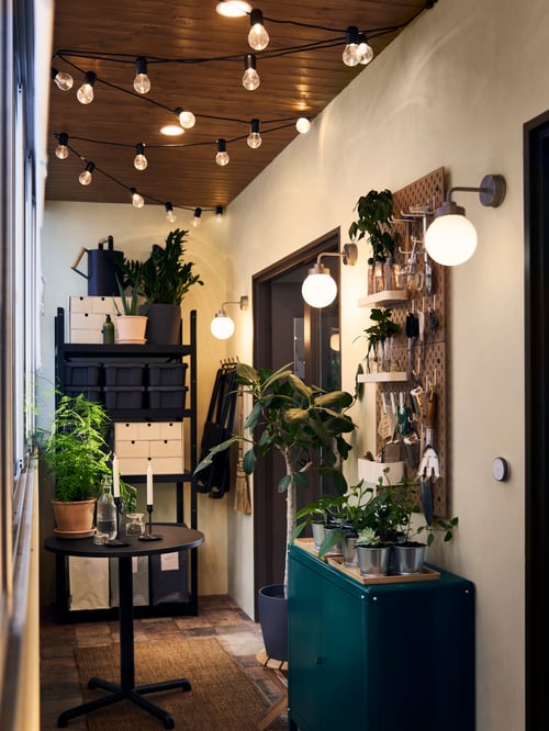 A green cabinet, a black table and BROR shelving unit, with FRIHULT wall lamps, lighting chains and ceiling spotlights.