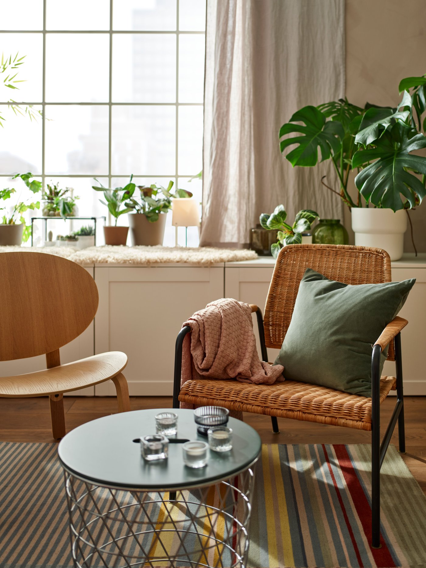 Salón con un sillón ULRIKSBERG beige con un cojín y una manta rosa junto a una mesa de almacenaje y un sillón.