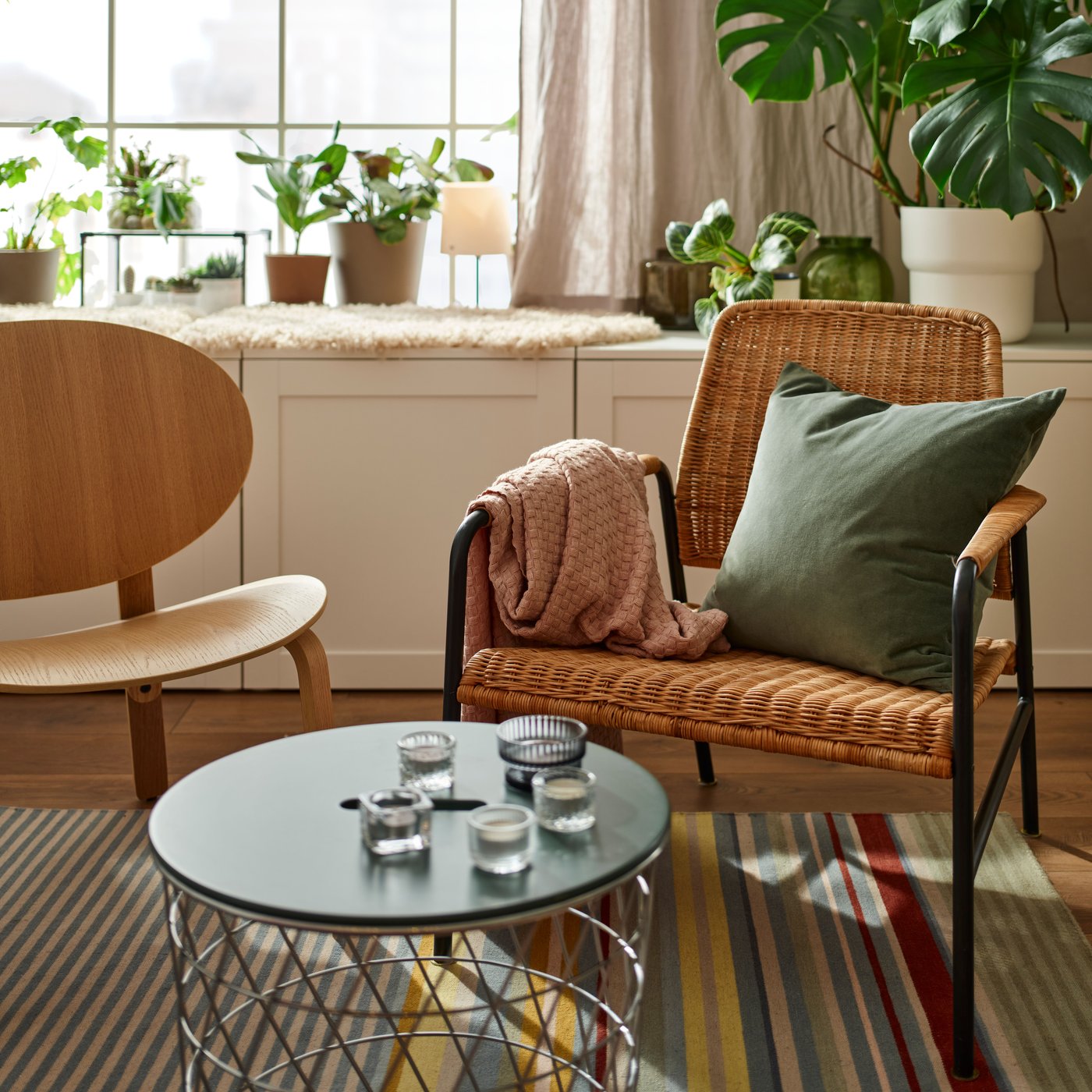 The ULRIKSBERG rattan armchair and the light wooden FRÖSET armchair in the living room on a striped rug.