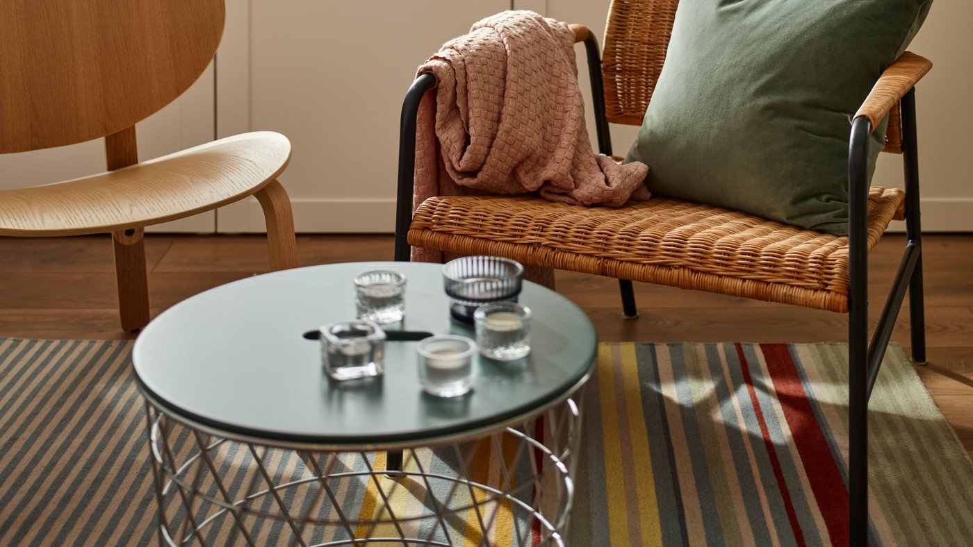 The ULRIKSBERG rattan armchair and the light wooden FRÖSET armchair in the living room on a striped rug.