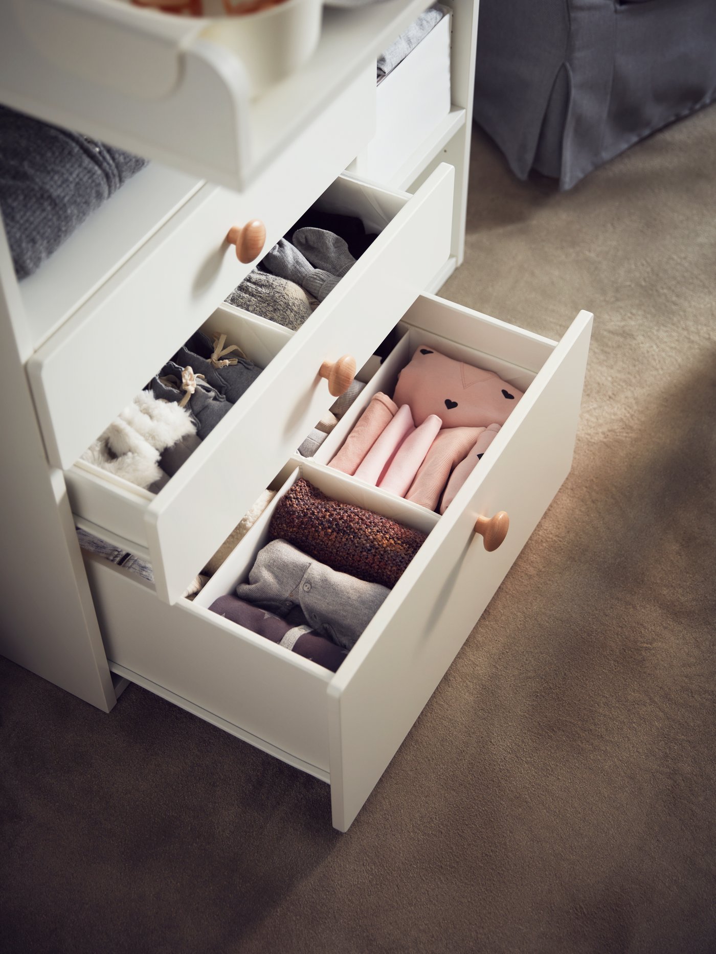 Offene Schubladen für Wickeltische mit weißen RASSLA Boxen und Fächern mit gefalteter Babykleidung.