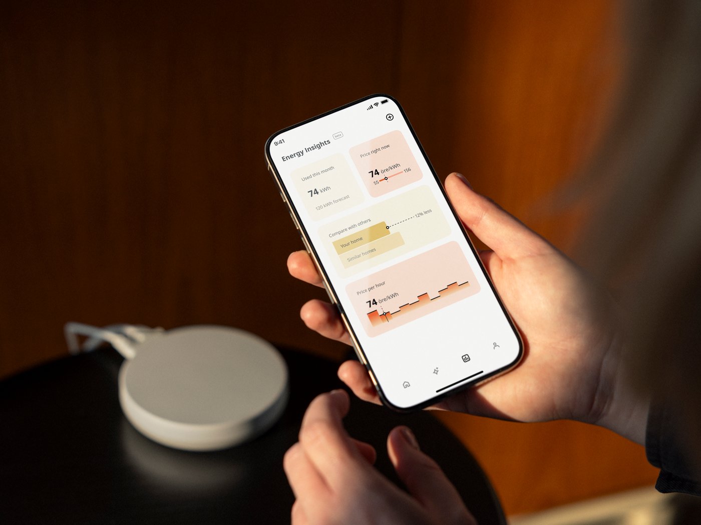 A person is holding a smartphone,  a DIRIGERA hub for smart products, is in the background.